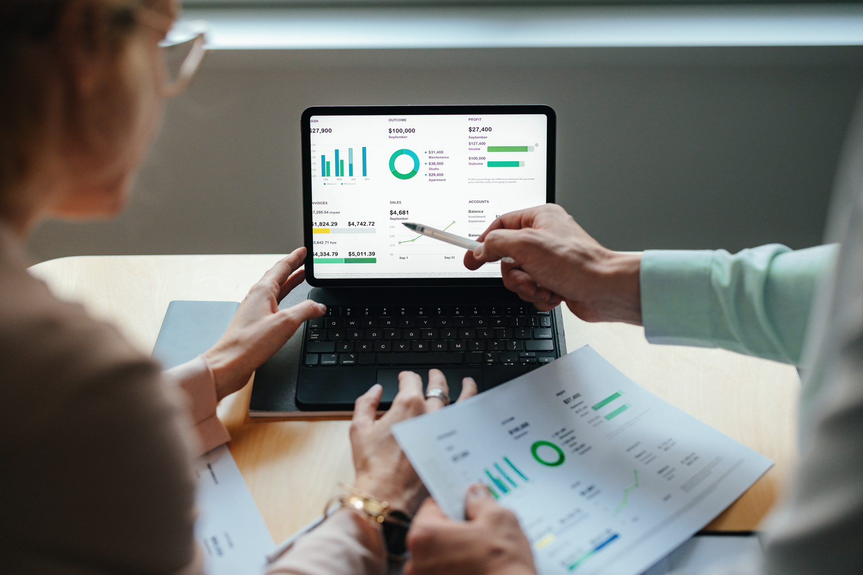 two people looking at charts on a laptop and piece of paper